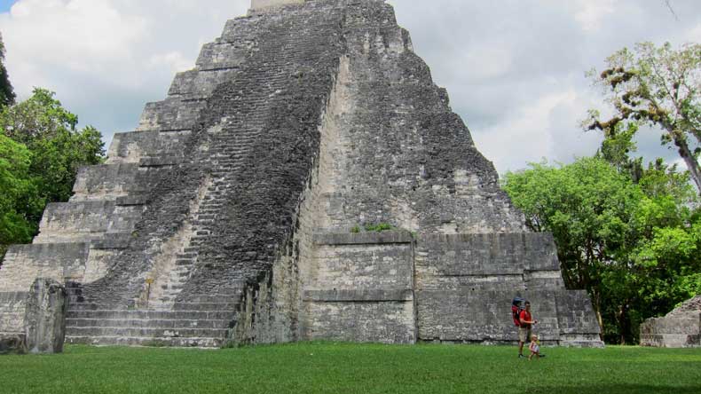 Father and toddler walking in front of a pyramid in Tikal National Park