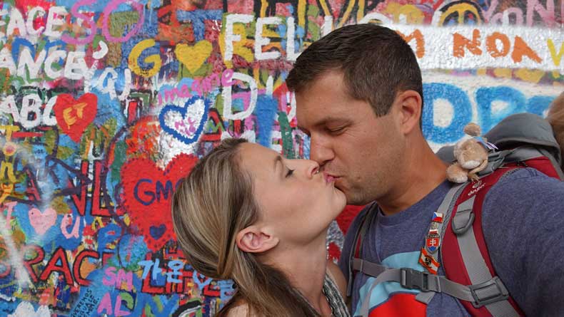 Couple traveling together kissing in front of the John Lennon Wall in in Prague Czech Republic