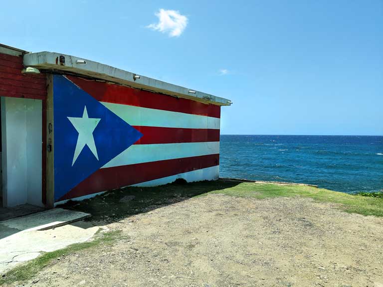 Puerto Rico flag painted on side of building with ocean in the background, found during road trip Puerto Rico