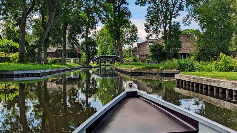 A boat in a quiet canal surrounded by homes on a day trip to Giethoorn from Amsterdam.