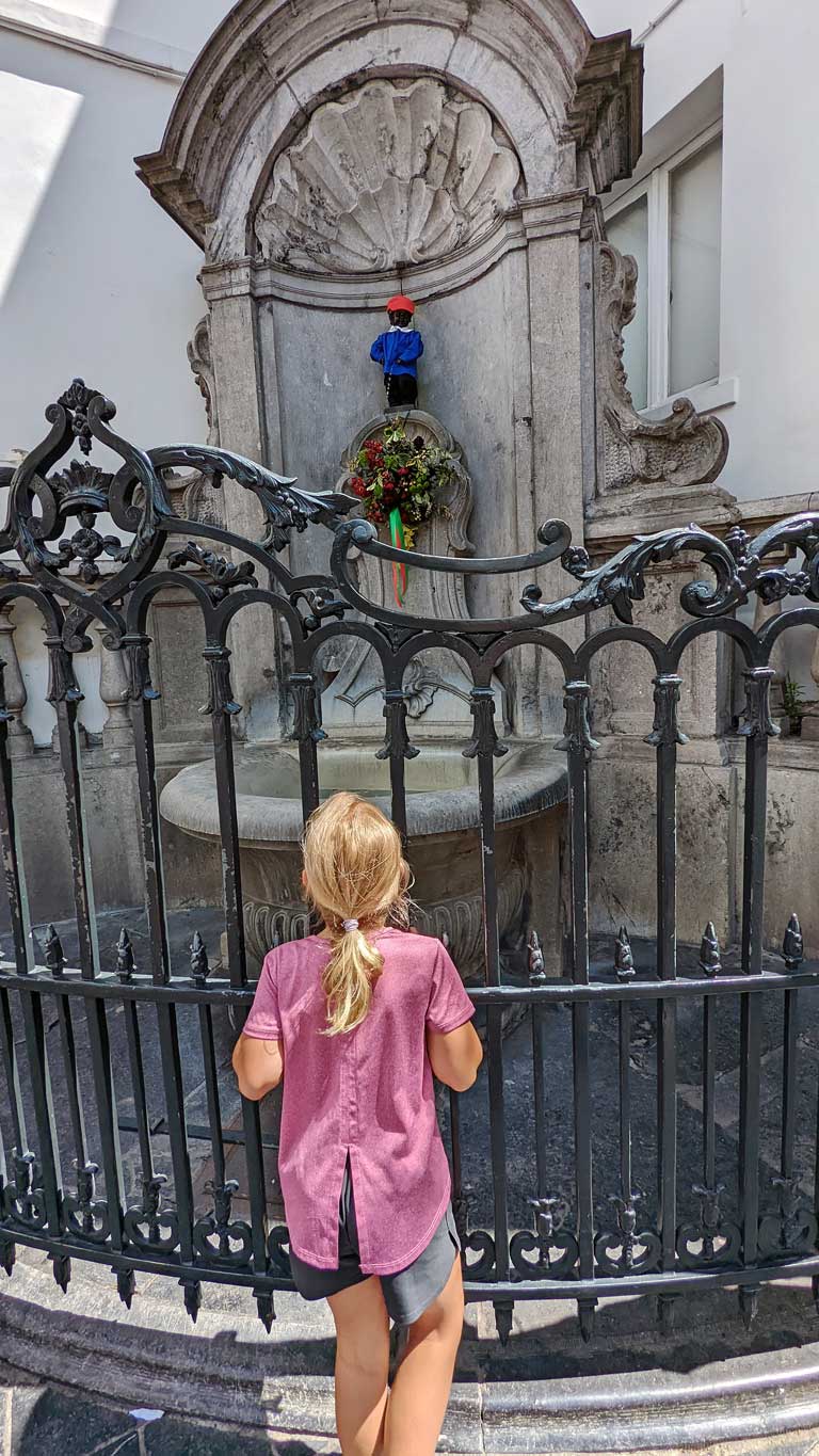 a little girl looking at Manneken Pis dressed in a costume