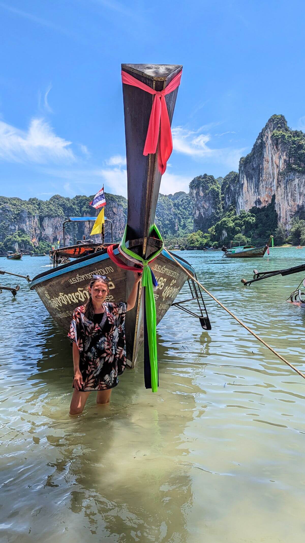standing in front of a longtail boat at one of the beaches Thailand is famous for