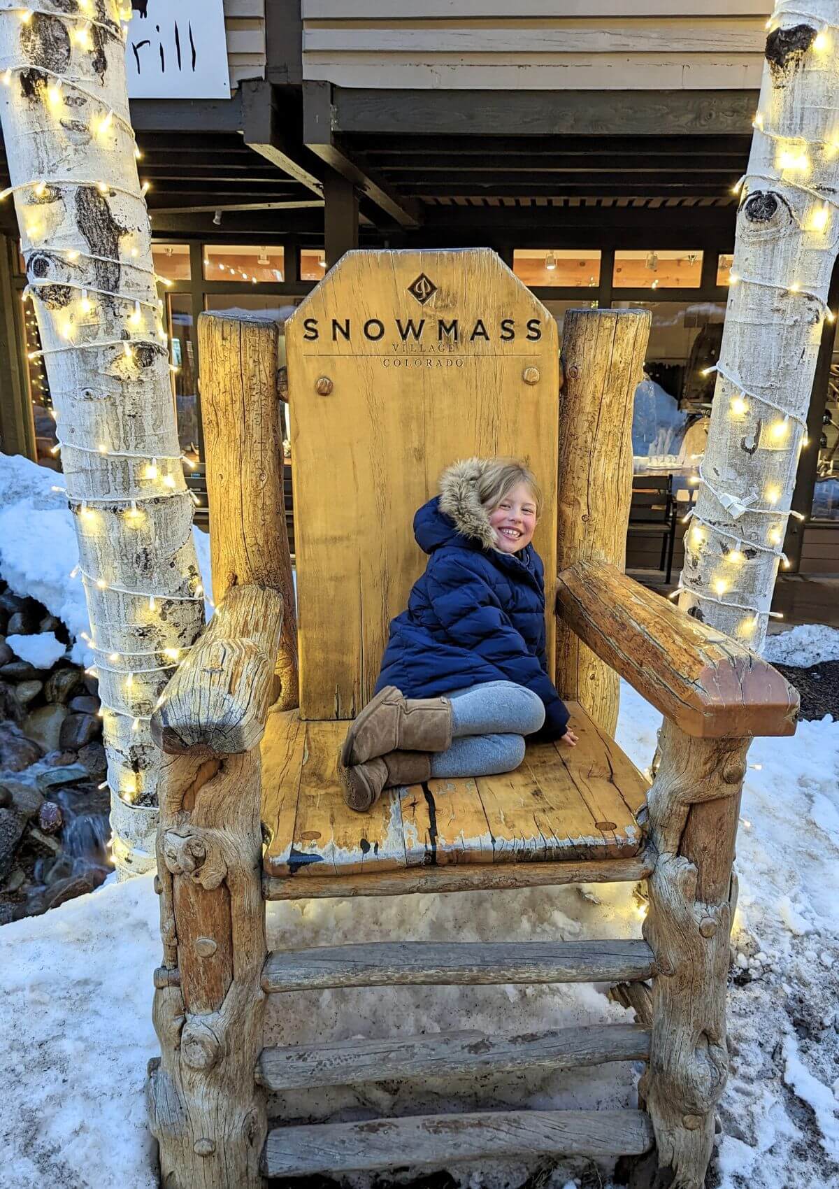 our daughter sitting in an oversized wooden chair that says Snowmass, Colorado